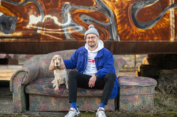 Stylish young man in blue old fashioned jacket, white hoodie and modern sneakers siiting on old...