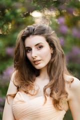 Romantic portrait of young beautiful girl standing in spring lilac garden
