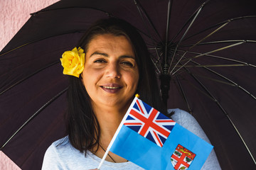  Woman with umbrella holds flag of Fiji in front of isolated wall background