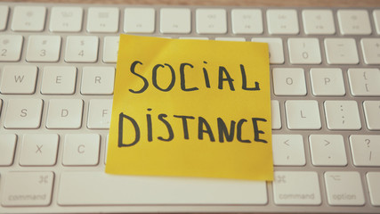 Social distance text inscription on yellow sticker reminder. White computer keyboard. Motivation for business, work from home.