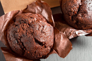 Tasty chocolate muffins in baked paper on black background, close-up