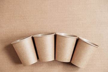 Disposable paper cups on kraft paper background. Eco friendly disposable tableware. Zero waste concept. Top view. Copy, empty space for text