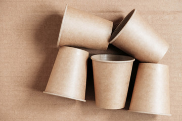 Disposable paper cups on kraft paper background. Eco friendly disposable tableware. Zero waste concept. Top view. Copy, empty space for text