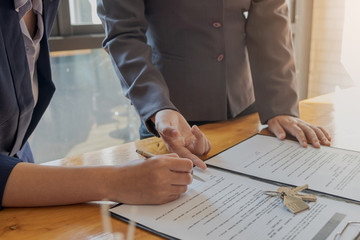 Customer signing a paper document for buying house. Estate agent pointing finger showing where to sign on wooden desk. Real estate, home loan and insurance concept.