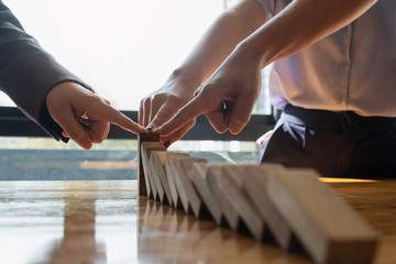 close up team businessman hand stopping falling wooden dominoes effect from continuous toppled or...