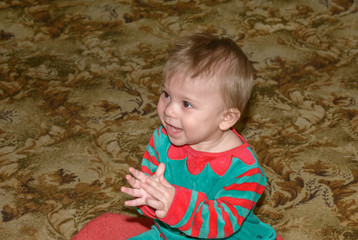 Fototapeta premium Baby boy in red-green suit is learning to play patty-cake.