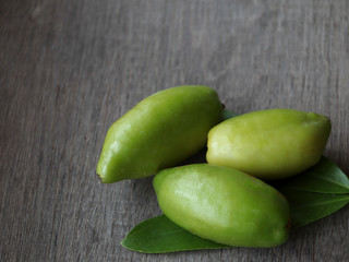 Three fresh green badam fruit on a wood grain floor.
