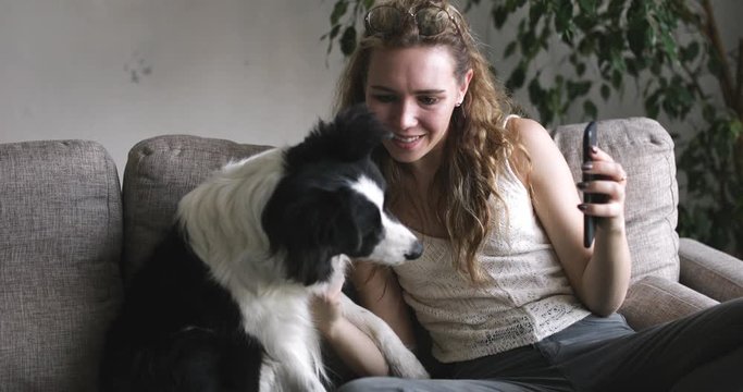 Side View of Young Woman Sitting and Petting Her Dog While Making Video Call on quarantibe in home. Attractive Girl Video Chatting, Smiling, Laughing, Talking. Online Communication Concept