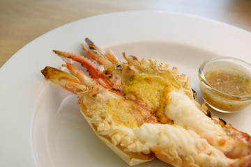 Grilled giant river prawn on white dish with spicy seafood sauce. Popular Thai food on wooden table as background