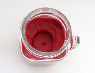 Aerial view of Raspberry aromatic candle in glass jar isolated on white background. Red burning candle in glass jar with lid to preserve fragrance.