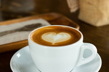 Hot coffee in a cup with foam milk beautiful art on wooden table background. Cappuccino or latte with froth foam, drinks concept.