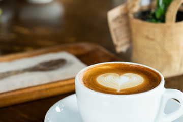 Hot coffee in a cup with foam milk beautiful art on wooden table background. Cappuccino or latte with froth foam, drinks concept.
