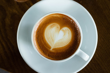 Hot coffee in a cup with foam milk beautiful art on wooden table background. Cappuccino or latte with froth foam, drinks concept.