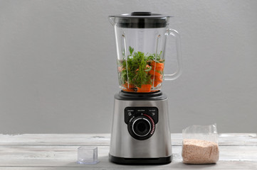 Blender, carrot, parsley, dill on a gray wooden table. Girl makes a smoothie of vegetables. Healthy lifestyle. Dietary nutrition. Carrots and greens close-up.