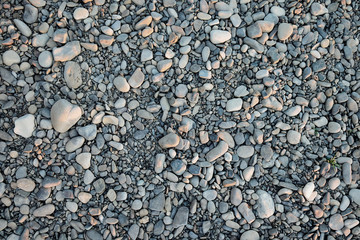 A closeup of a pile of loose rounded gray stones lying on a riverbank.  The rounded stones create an abstract pattern which is well usable for backgrounds and textures, resembling solid.