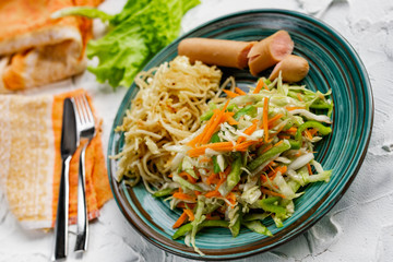 Salad of fresh vegetables on a plate with leaves, next to toasted pasta spaghetti with egg and meat sausage, a Hearty lunch, everyday productsfor a home dinner