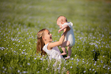 Fototapeta premium Portrait of happy little sisters who are looking at each other in a linen field.