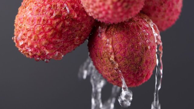 Water splashing on lychee in slow motion. Close-up fresh lychee on dark background. Red exotic fruits