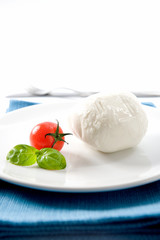 buffalo mozzarella from Campania and tomato with basil on a white background and placed on a blue napkin