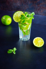 Mojito cocktail with lime and mint in tall glass. Fresh mojito in glass on a dark background. Refreshing mint cocktail with lime. Infused water