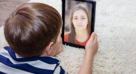 A young person or child who uses a digital tablet to make video calls to friends, family, or a...