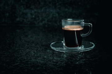 Front view of glass cup with creamy coffee, grey and dark background.
