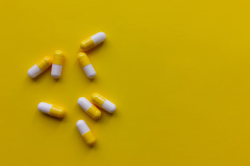 Yellow and white capsules and white pills on a yellow background. 
