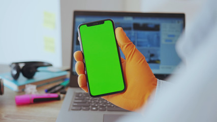 NEW YORK - March, 28, 2020: Young adult businessman using a smartphone tapping on vertical chroma key mock-up display working by computer in his house. People at home. Technology. Quarantine.