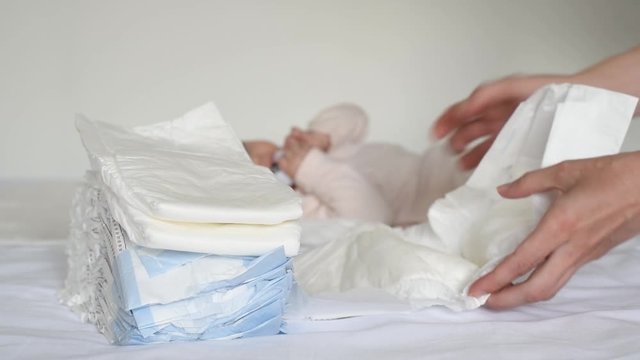 A young mother holds a white diaper in her hands and looks at it, in the background a small child