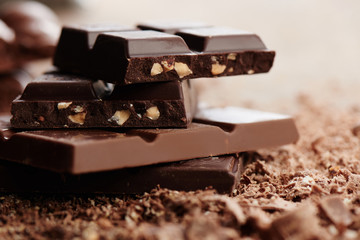 Composition of bars and pieces of different milk and dark chocolate, grated cocoa on a brown background side view close up