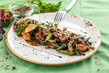 Plate of asian chicken salad with bean, pepper and sesame seeds on green background