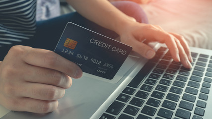 Women hands holding a blue credit card and typing CVV numbers on a computer keyboard. Payment for online shopping or internet banking at home. Select focus point on a credit card.
