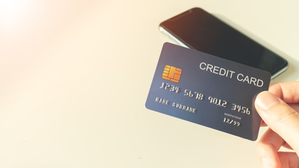 Women hands holding a blue credit card with a smart phone background. Payment for online shopping or internet banking and select focus point on a credit card.
