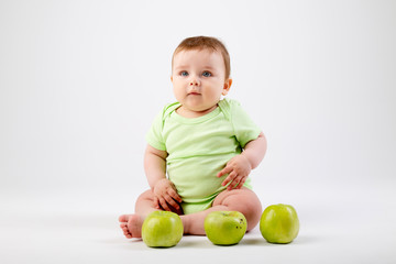 Fototapeta na wymiar Cute toddler in green bodysuit sits with green apples on white background