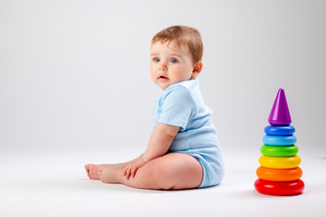 Cute baby in blue bodysuit plays with multi-colored pyramid on a white background, space for text