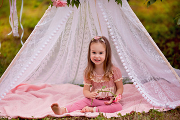 Fototapeta na wymiar Portrait of a cute happy little girl 3-4 years old in the summer in the park in an openwork floral wigwam.