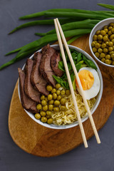 Asian traditional soup in a bowl on a wooden stand. Beef pho bo with eggs and green peas. Top view.