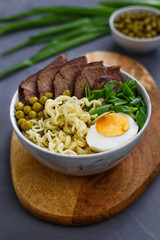 Asian traditional soup in a bowl on a wooden stand. Beef pho bo with eggs and green peas. Top view.