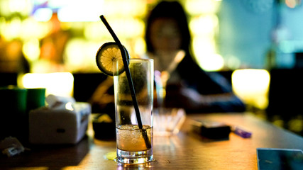 A yellow cocktail in a glass with a black straw and lemon slice at the bar, evening time, half-drunk alcohol drink in a pub, restaurant, grain film effect