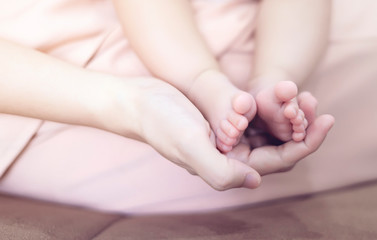 close up mother holding new born baby toddler feet in her palm, warm love and caring for child in motherhood and parenthood, mom looking after baby playing having bonding and touching cleaning feet