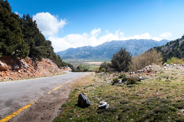 A lonely deserted road leads through the mountains or highlands on the Greek island of Crete. The road loses itself on the horizon. White clouds can be seen in the sky.