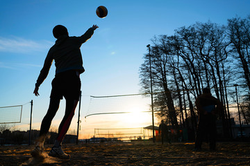 Silhouettes of three men playing beach volleyball,