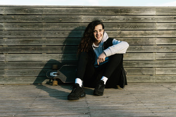 Obraz premium Teenage girl sitting on a longboard, leaning against a wooded wall