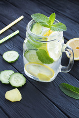 Sassy  water  slimming or infused water with lemon, cucumber and ginger in the glass on the black wooden  background. Location vertical.