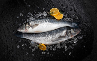 Seabass fish on ice on black stone background, top view