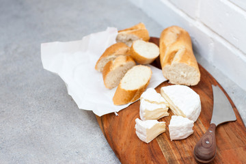 Still life with baguette and camembert cheese on rustic wooden board. White background, lot of copy space.