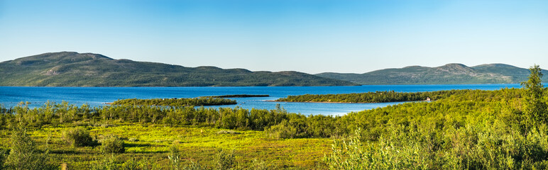 Summer landscape with green medow and lake, forest and village on horizon near Sangis in Kalix Municipality, Norrbotten, Sweden. Swedish landscape in summertime.