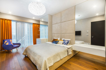 Fototapeta na wymiar A fashionable brand-new bedroom with wide panoramic window. Mirrors and design armchai