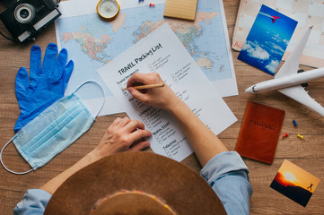 Young woman in hat writing packing list on wooden background