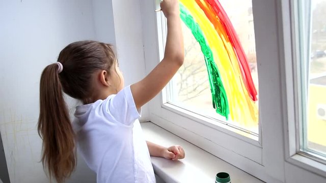 Child graws a rainbow on the window during Covid-19 quarantine at home. Chase the rainbow flashmob and staying at home concept
